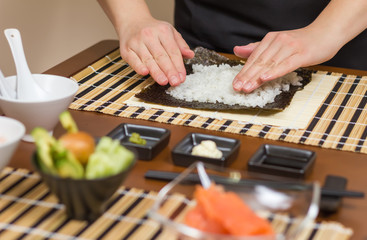 Woman chef filling japanese sushi rolls with rice