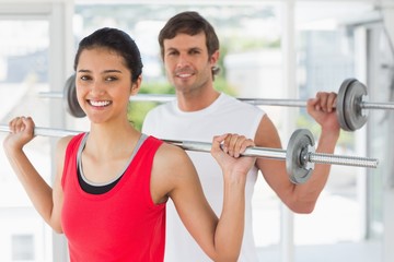 Fototapeta na wymiar Fit young couple lifting barbells in gym