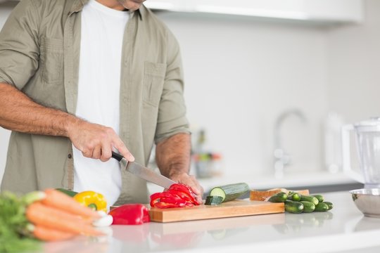 Mid section of a man chopping vegetables in kitchen
