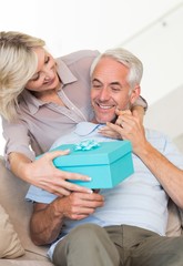 Obraz premium Smiling woman surprising mature man with a gift on sofa