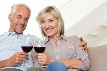 Smiling mature couple with wine glasses sitting on sofa