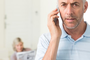 Mature man using cellphone with woman reading newspaper