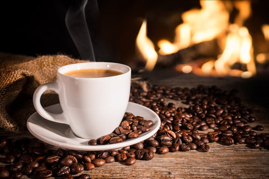 Cup of hot coffee and coffee beans near fireplace