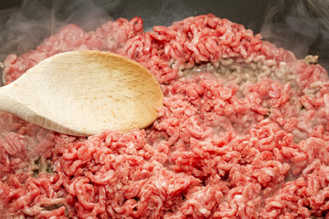 Raw mince starting to brown in pan with wooden spoon