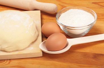 Eggs, dough, flour on wooden board