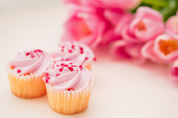 Cupcakes with pink cream,heart sprinkles and tulips on white tab