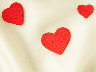 Red wooden decorative hearts on white silk background.