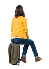 back view of walking  woman  in cardigan sits on a suitcase.
