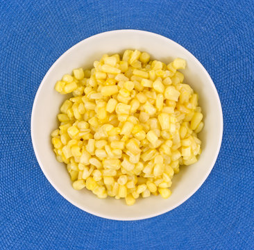 Buttered small shoepeg corn in a bowl on a blue placemat