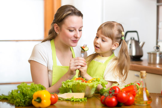 mother feeding kid vegetables in kitchen