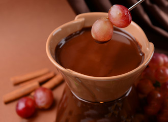 Chocolate fondue with fruits, on  brown background