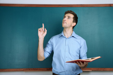 Young teacher near chalkboard in school classroom