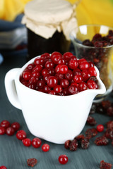 Fresh and dry cranberry in pitchers on wooden table close-up