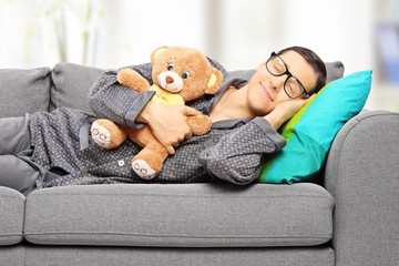 Young man holding teddy bear and taking a nap on couch