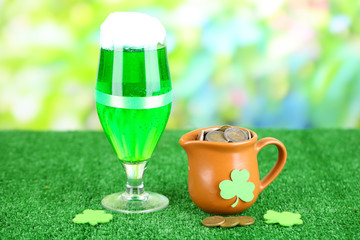 Glass of green beer and pitcher with coins