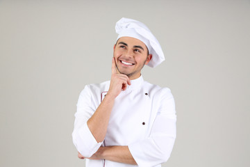 Professional chef in white uniform and hat, on gray background