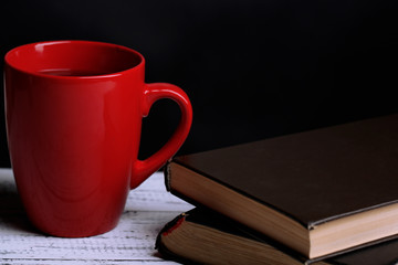 Cup of hot tea with books on table on dark background