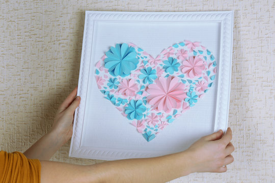 Woman hanging up picture with heart from paper flowers