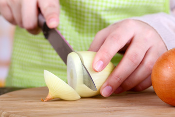 Female hands cutting bulb onion, on kitchen background