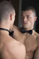 Shirtless young man with bow-tie looking at reflection in mirror