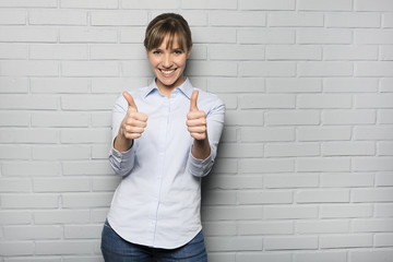 Happy Young Woman Showing Thumbs Up Sign isolated over a wall