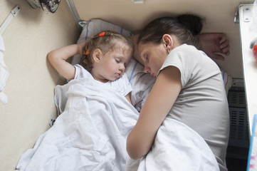 Мама и дочка спят на койке в вагоне поезда - obrazy, fototapety, plakaty