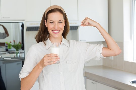 Happy woman flexing muscles while drinking water in kitchen