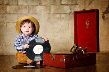 Little boy sitting with a plate near the gramophone.