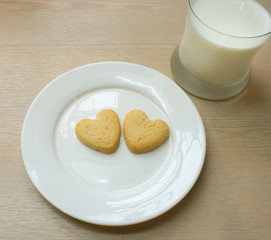 Heart cookies on white plate and glass of milk.
