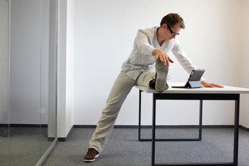 leg exercise durrng office work - man with tablet in his office