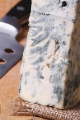 Blue cheese on a kitchen board and knife. vertical macro.