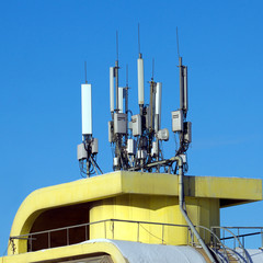 Electronics aerials on yellow building top over blue sky