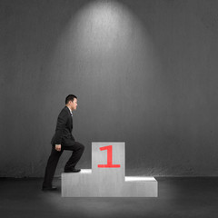 Businessman climbing on podium with spot light, interior