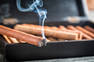 Closeup of burning cigar on wooden humidor