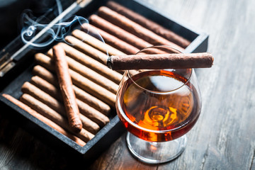 Burning cigar on humidor and cognac in glass