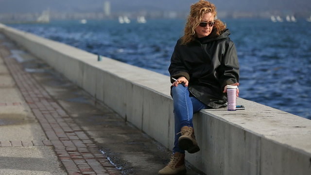 lonely blonde women smoke and drinking coffee at near ocean