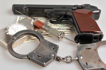 Drugs, syringe with blood, pistol, handcuffs and money on gray