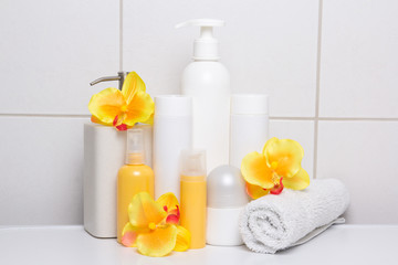 Obraz na płótnie Canvas set of white cosmetic bottles with orange flowers over tiled wal
