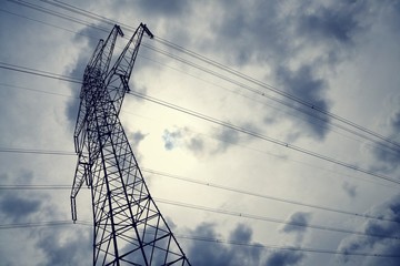 Electricity pylon against sun behind clouds