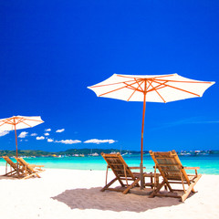 Wooden chairs and umbrellas on white sand beach facing the