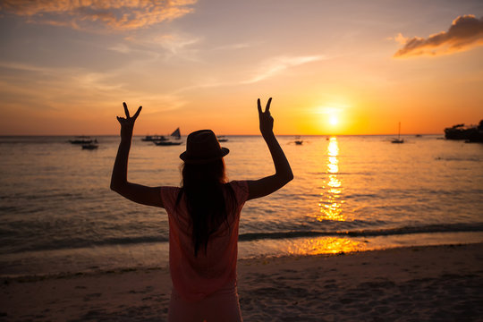 Silhouette of a young woman with raised hands at sunset on the
