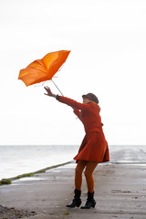 Broken Orange umbrella is flying from the girl.