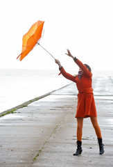 Broken Orange umbrella is flying from the girl.