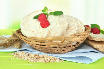 Tasty crispbread with berries in wicker basket, on green table