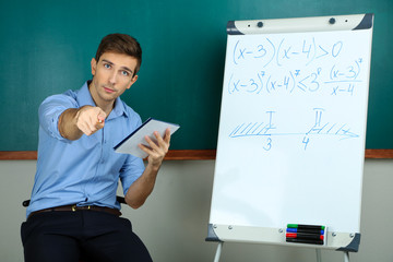 Young teacher sitting near chalkboard in school classroom