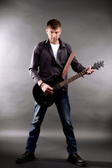 Fototapeta premium Young musician playing guitar on gray background