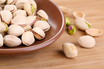 Pistachio nuts on plate on wooden background