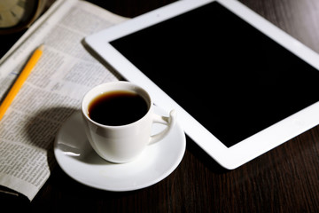Tablet, newspaper, cup of coffee and alarm clock on wooden