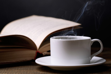 Cup of hot coffee with book on table on dark background