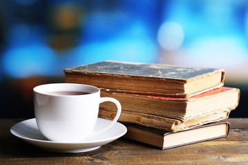 Cup of hot tea with books on table on bright background